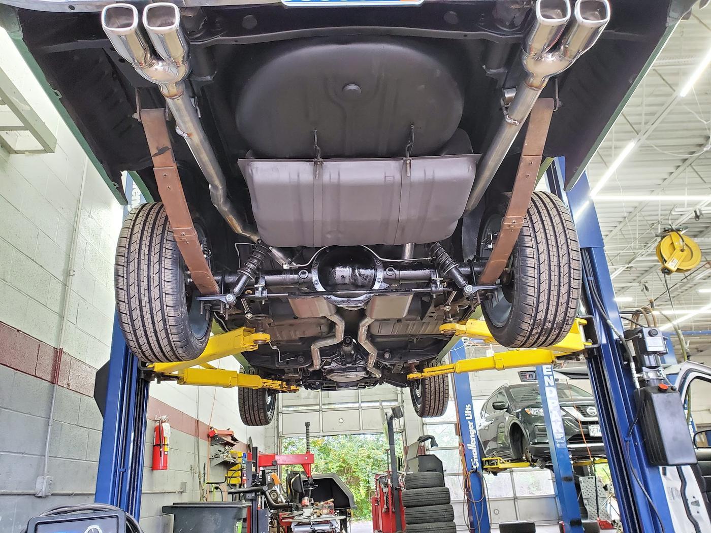 The underside of a restored classic car on the lift, twin exhaust gleaming
